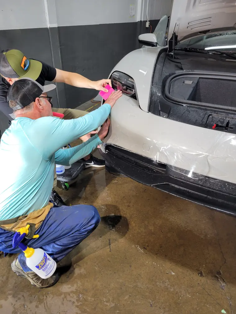 Installer squeegeeing XPEL film onto the front bumper of a white Porsche in the install bay